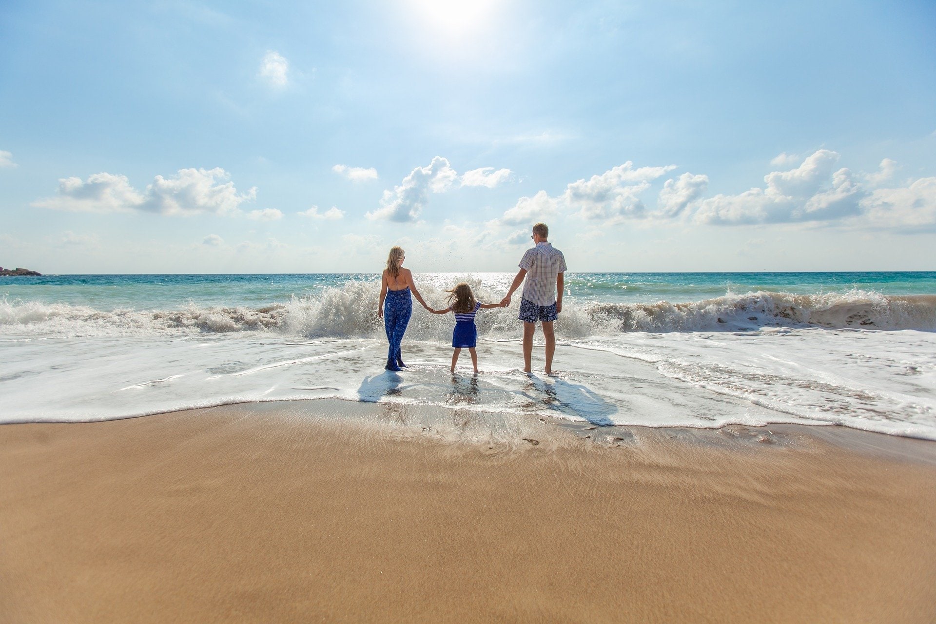 Pai, mãe e filho de mãos dadas no mar durante suas férias em família.