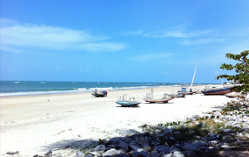 imagem da praia de Flecheiras em fortaleza. A imagem mostra um céu azul, uma areia clara, alguns barcos e pedras.