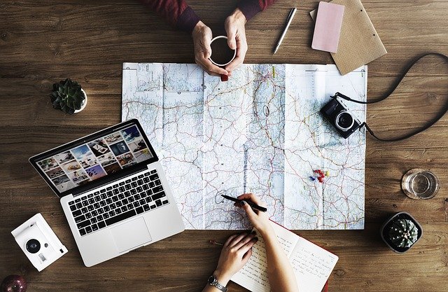 mãos desenhando e planejando sua viagem em cima de mapa com computador ao lado.