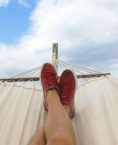 pés com tênis vermelho repousados em uma rede de descanso.