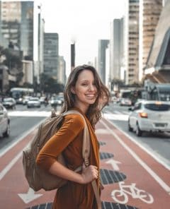 Mulher, de lado, com uma mochila nas costas, sorrindo enquanto está na ciclofaixa da avenida paulista.