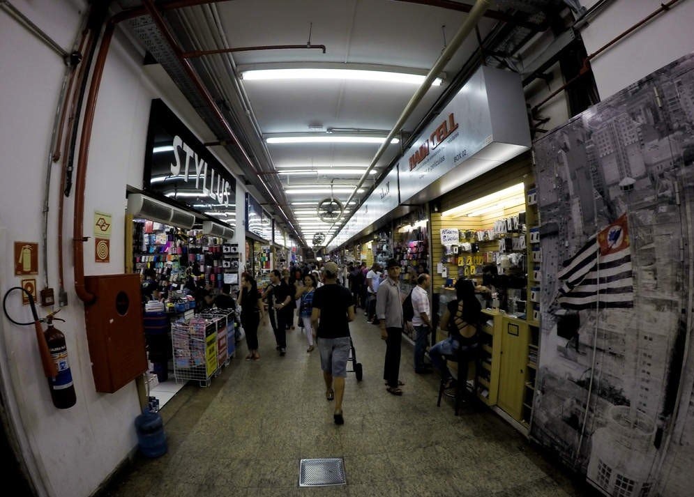 Pessoas em um corredor de um Shopping da 25 de março olhando as lojas e seus pertences.